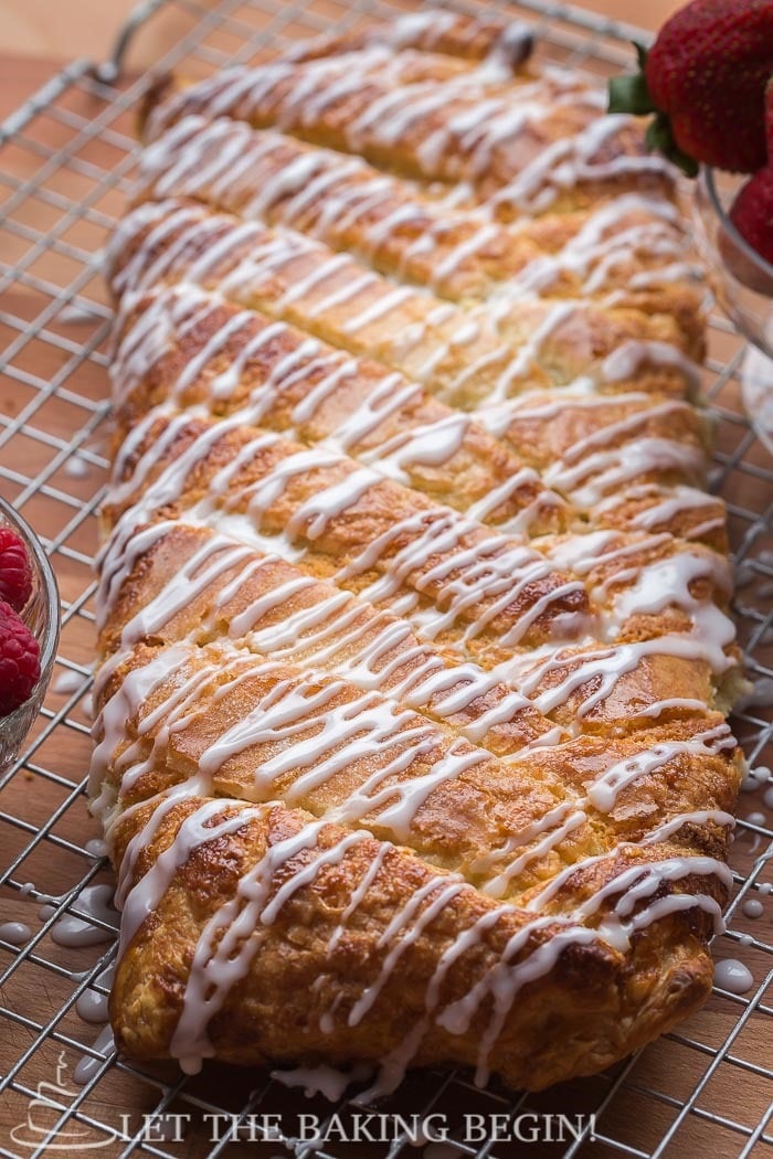 Puff pastry braid topped with a powdered sugar glaze on a cooling rack.