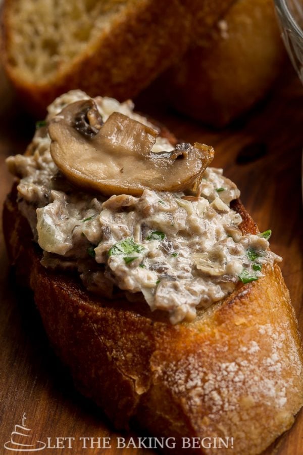 Mushroom pate spread over a piece of toasted baguette with a mushroom on top