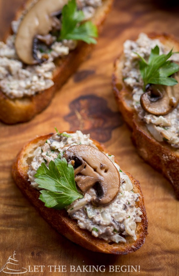 Mushroom pate spred over toasted baguettes all lying on a wooden cutting board.