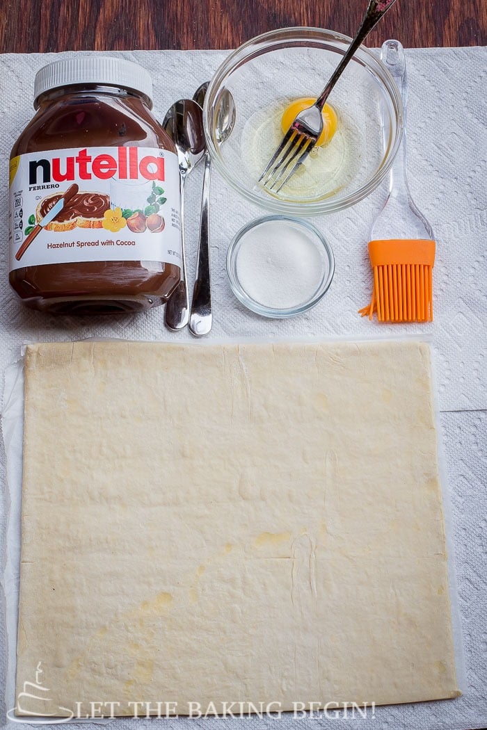 Nutella, egg wash and a puff pastry sheet on a paper towel.