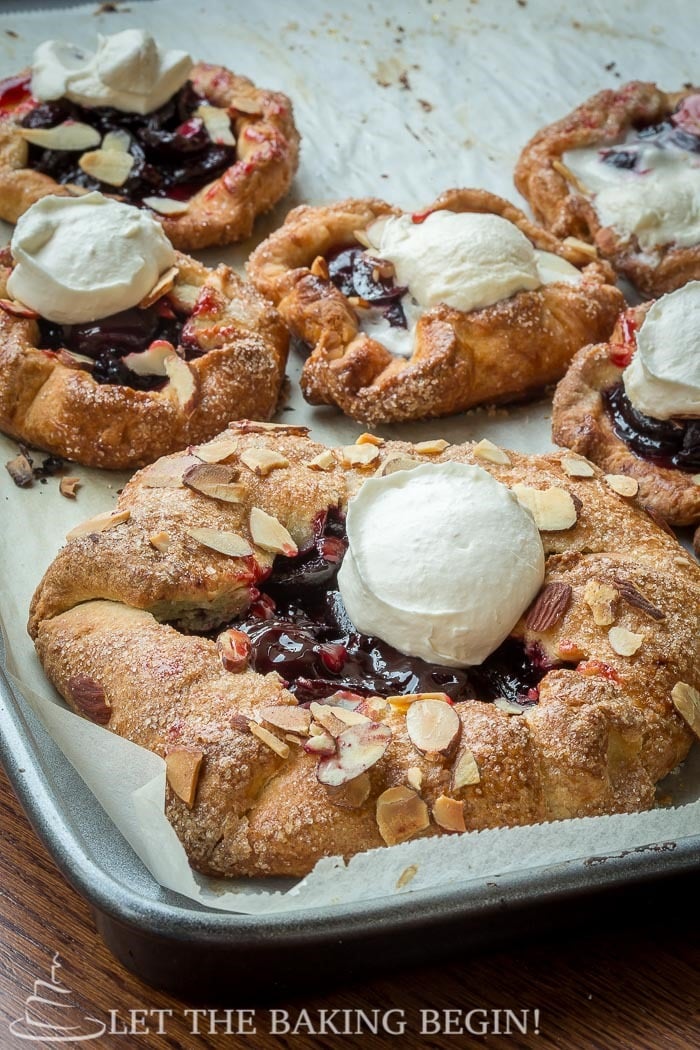 Cherry galettes with whipped cream and almonds on a baking sheet with parchment paper. 