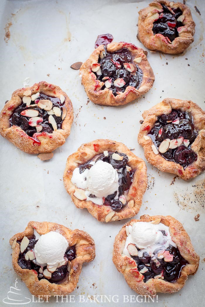 Cherry galettes topped with almonds on baking sheet. Some topped with whipped cream.