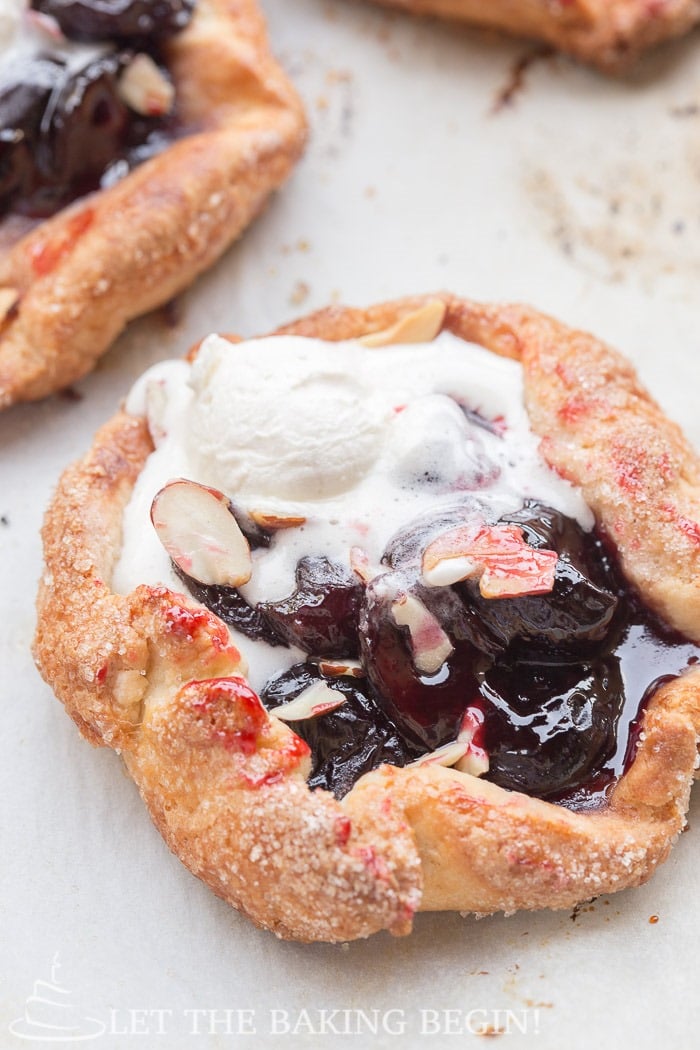 Cherry galette with homemade sweet whipped cream and almonds on parchment paper.