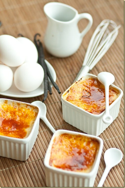 Classic creme brulee in white ramekins next to a whisk, spoons and a plate of eggs.