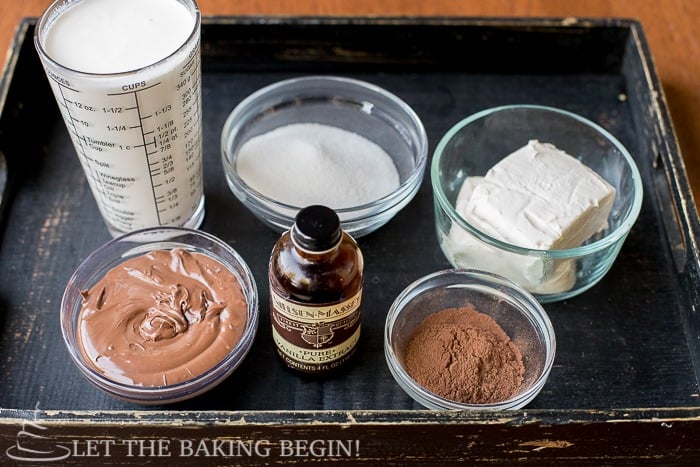 Bowl of heavy cream, sugar, cream cheese, nutella spread, cocoa powder, and vanilla extract in a wooden tray.