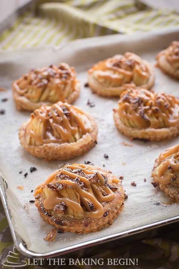 Puff pastries with sliced apples drizzled with dulce de leche on a baking sheet. 