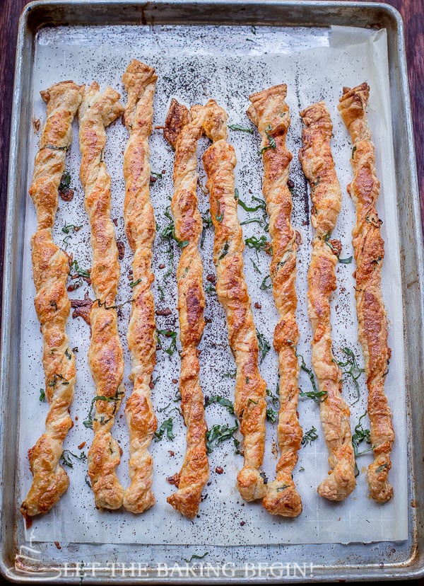 Pastry twists topped with paprika and fresh greens in a parchment lined baking sheet.