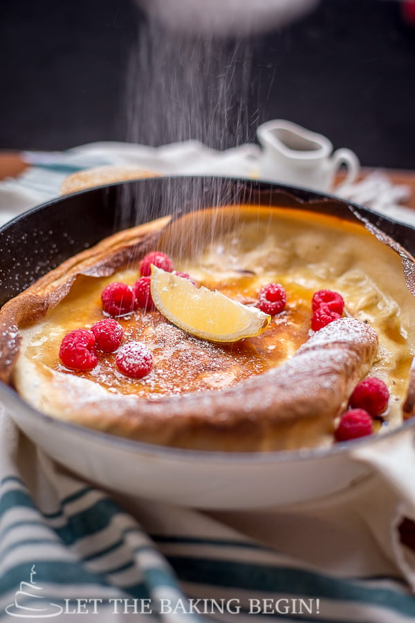 German pancake topped with raspberries, lemon, syrup and powdered sugar in a pan. 