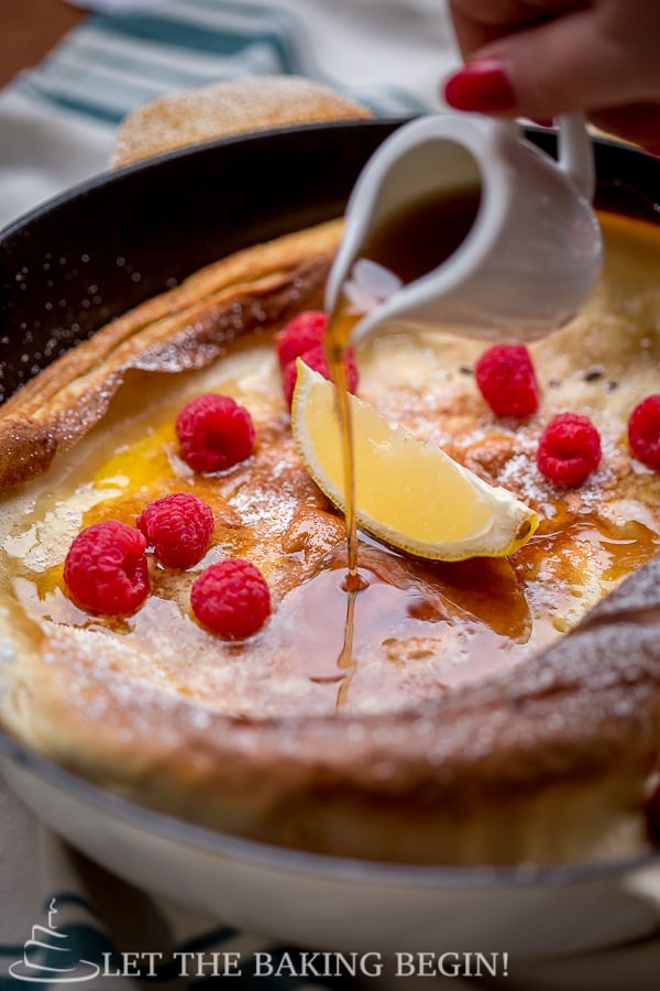 German pancake topped with raspberries, lemon, and syrup.
