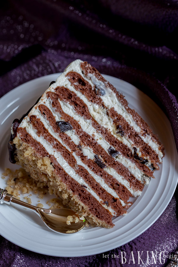 A slice of chocolate cake with layers of sour cream frosting and dried plums on a plate. 