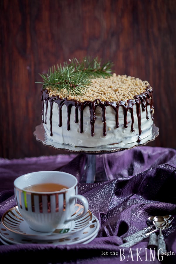 Chocolate cake with plums, walnuts and sour cream on a cake stand next to a cup of tea. 