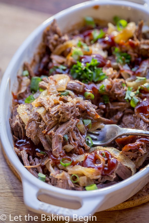 Soft and tender pot roast in a casserole dish on a fork with onions and barbecue sauce.