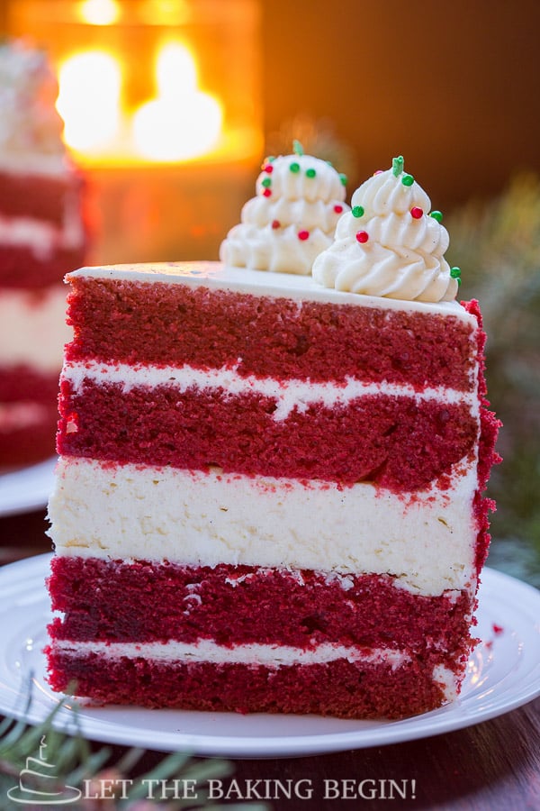 Slice of red velvet cheesecake cake on a white plate topped with frosting and sprinkles.