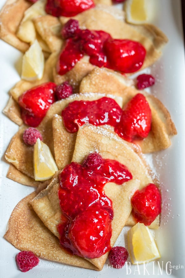 Crepes topped with strawberry and raspberry sauce and lemons.