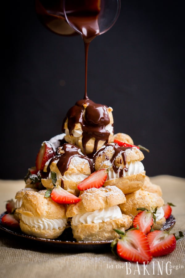 Cream puffs topped with strawberries, chocolate, and powdered sugar on a black decorative plate.
