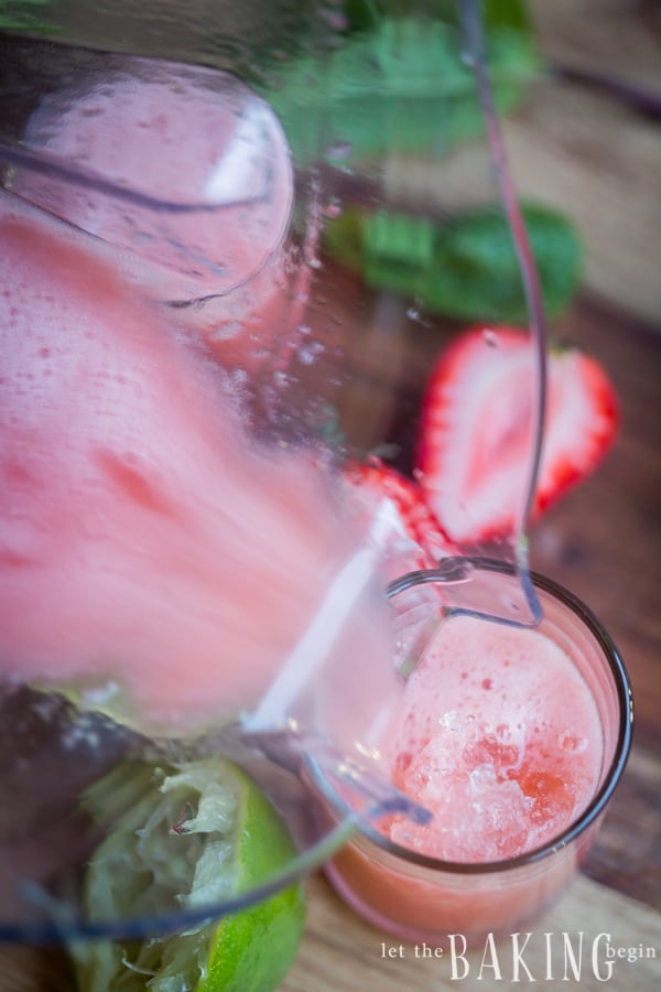 Strawberry-Mint Limeade being poured into a glass next to strawberries and mint leaves. 