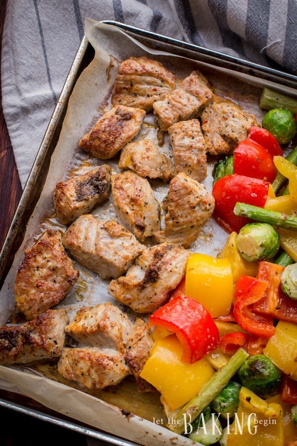 Baked vegetables and pork on a parchment lined baking sheet. 