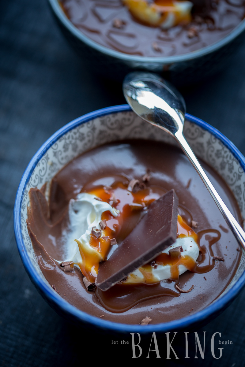 A bowl of coffee and chocolate pot de crème topped with caramel sauce and a metal spoon. 