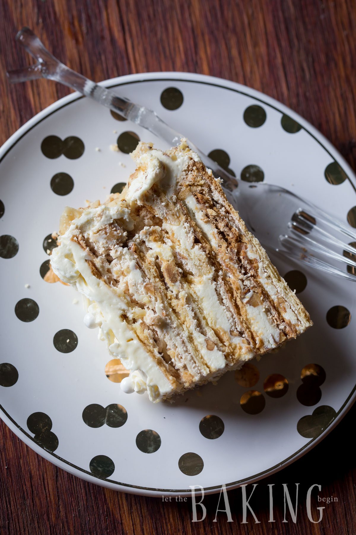 A slice of shortbread cake with layers of meringue and walnuts on a plate with a fork. 