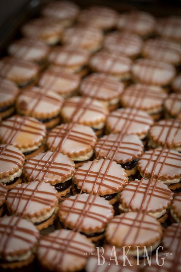 Plum Butter Cookies laid out on a baking sheet topped with icing and chocolate drizzle.