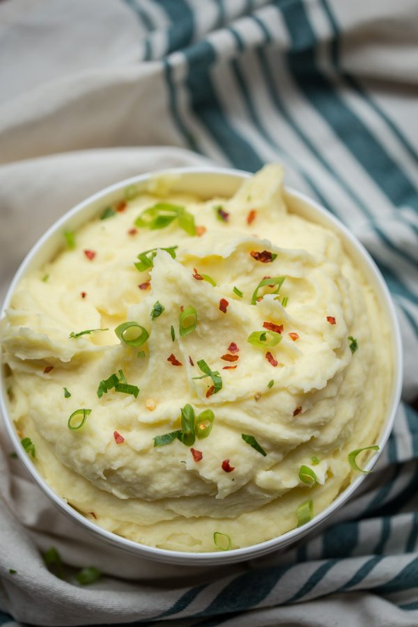 Bowl of mashed potatoes topped with chili pepper flaeks and green onions.