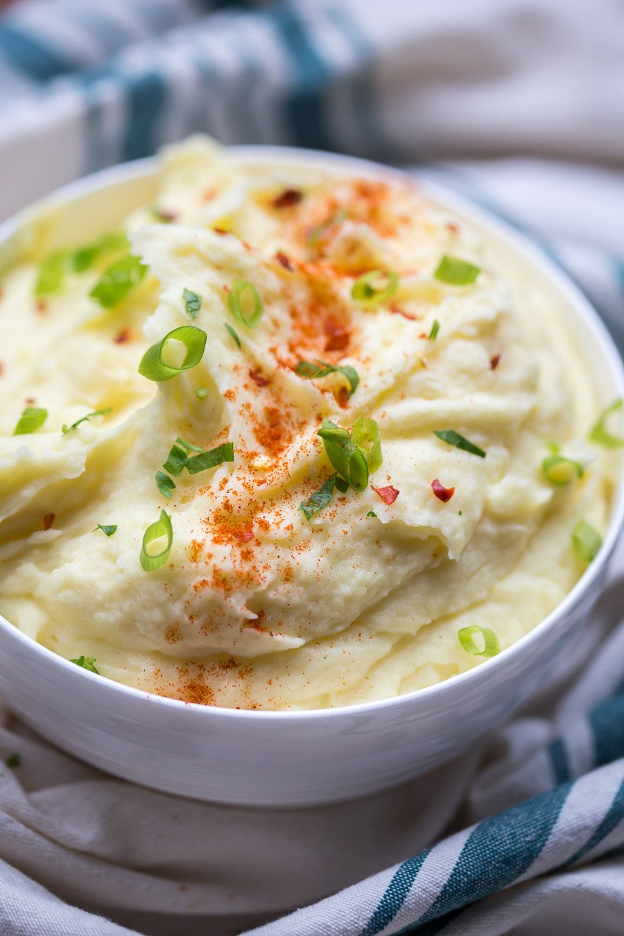 Bowl of fluffy mashed potatoes in a bowl with sliced green onions and a sprinkle of paprika