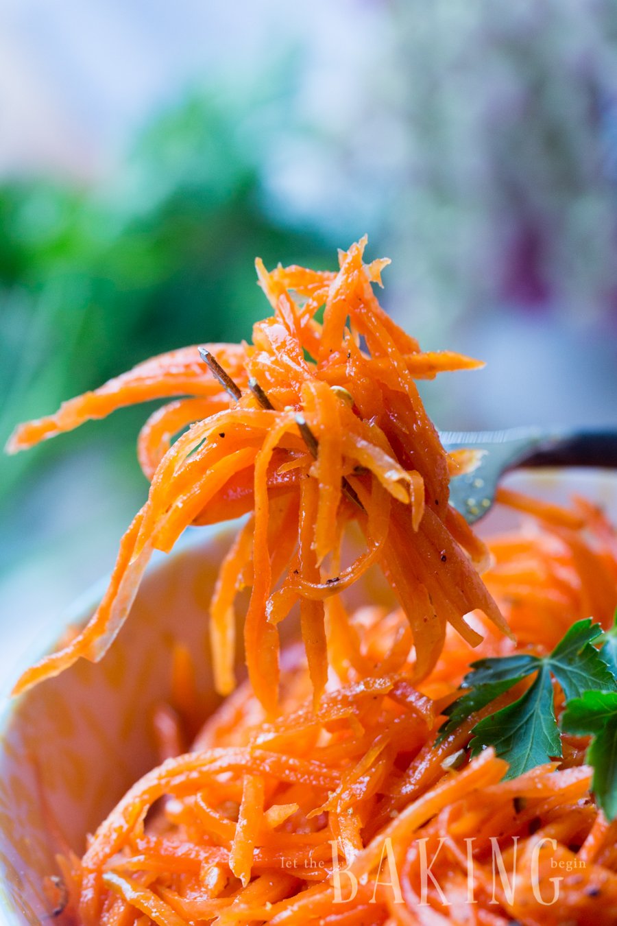 Spicy Korean Carrots on a fork next to a bowl of carrot salad.