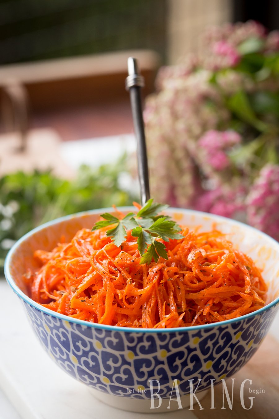 Spicy Korean carrots in a bowl with a metal spoon topped with parsley and grated black pepper.
