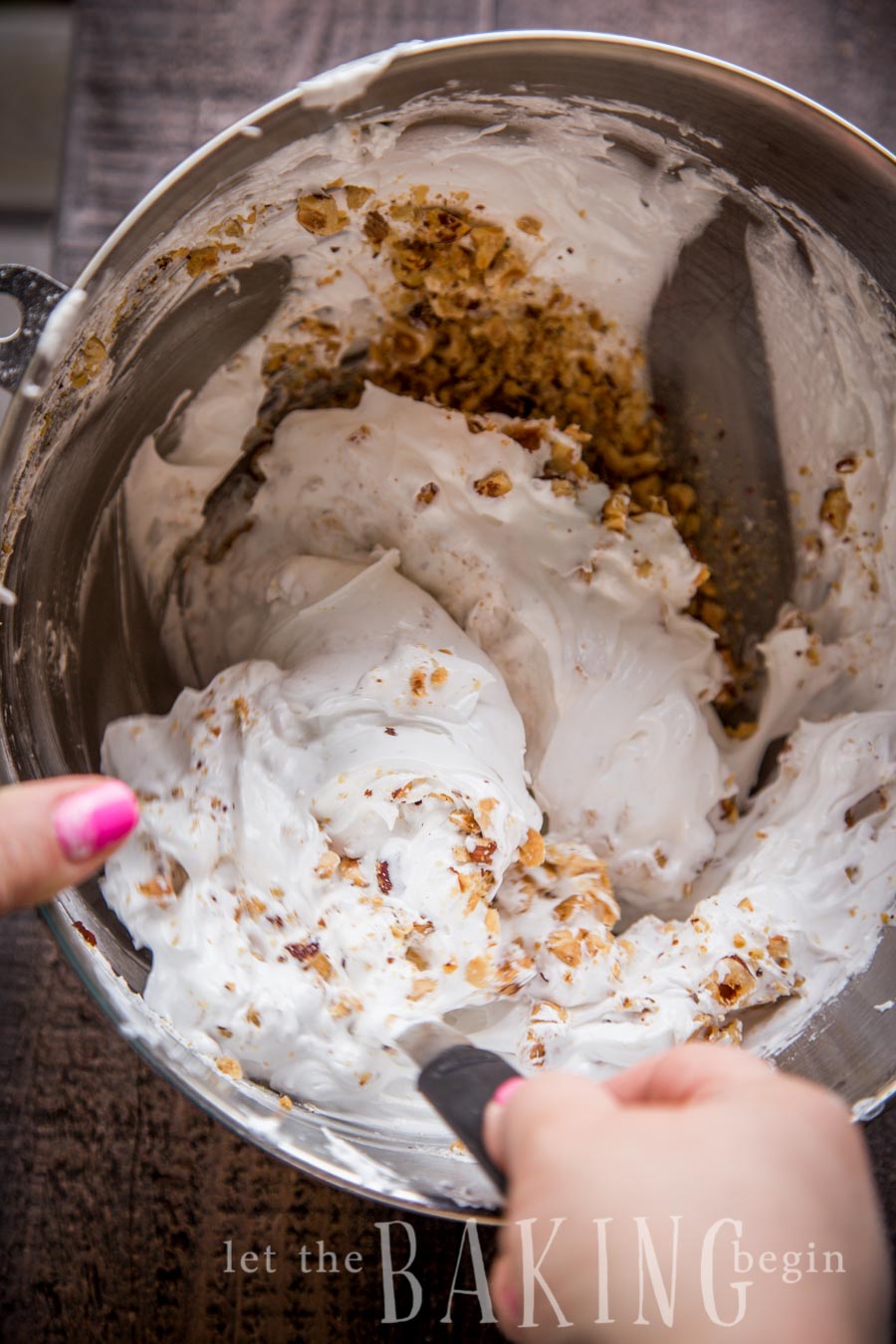 Meringue with hazelnuts in a mixing bowl being mixed with a spatula.
