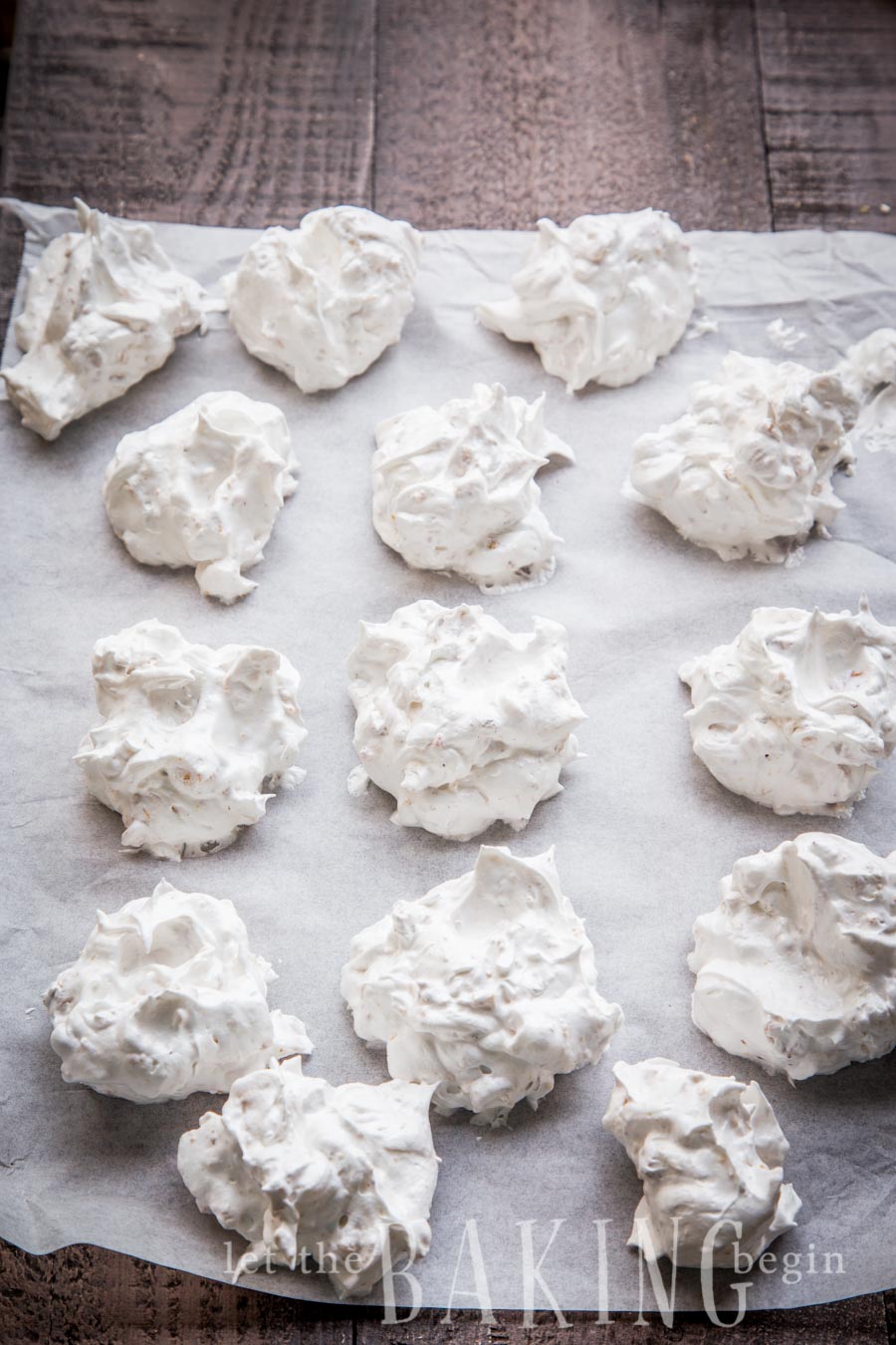 Spooned out hazelnut meringues on a parchment paper on a wooden table.