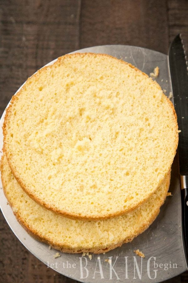 Sliced yellow sponge cake on parchment paper with a knife.