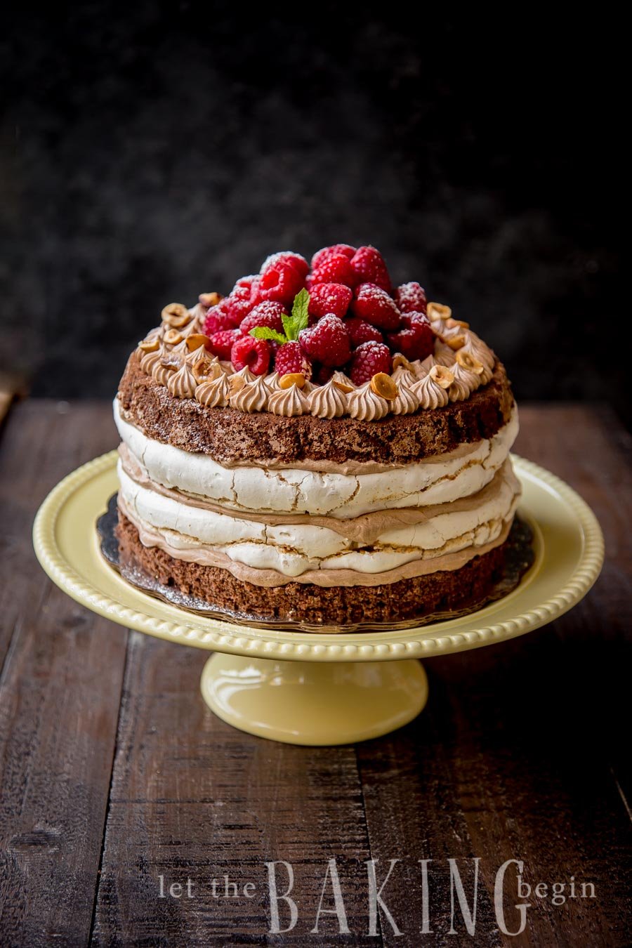 Hazelnut meringue Nutella cake on a yellow cake platter topped with raspberries. 