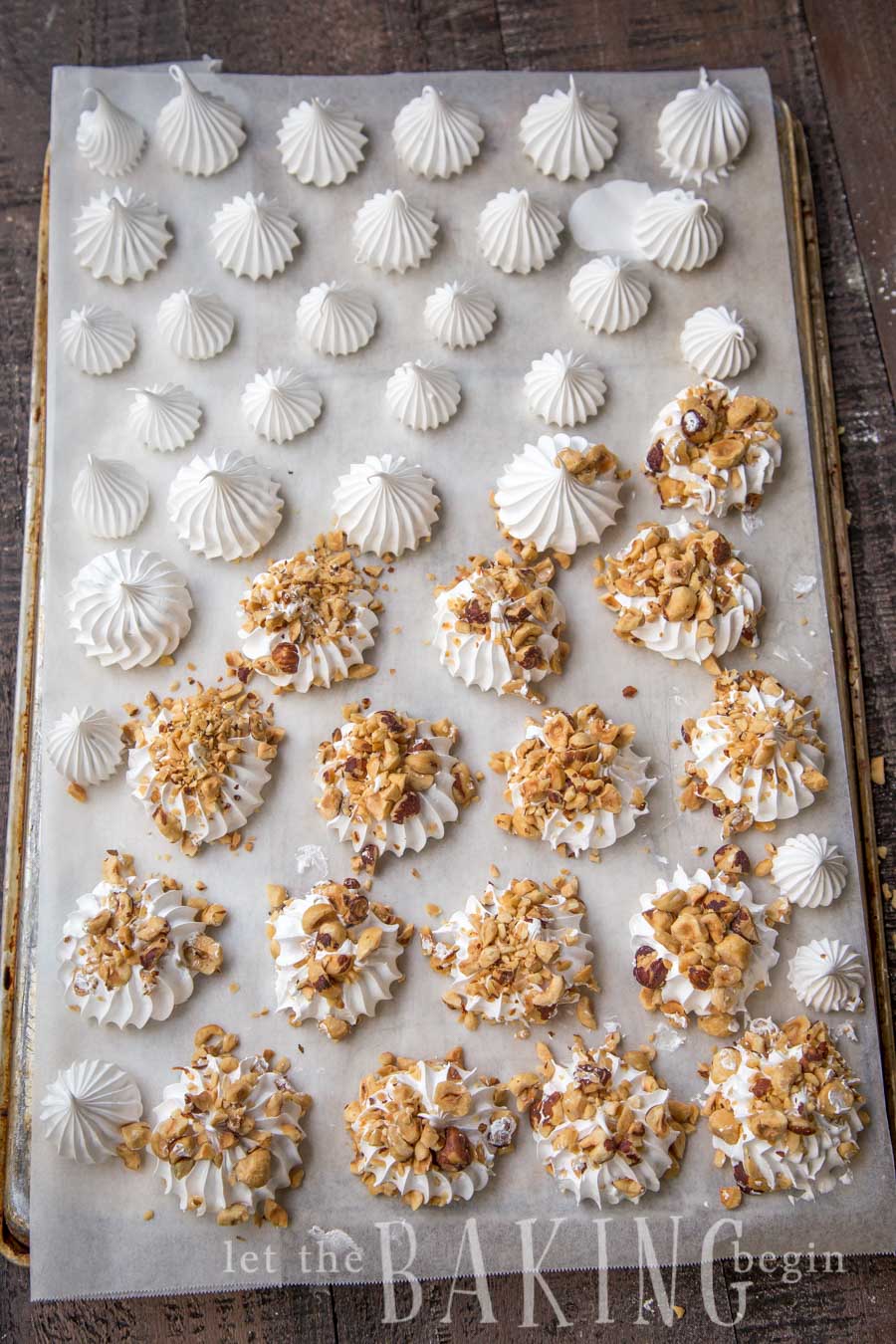 Half meringues on a parchment-lined a baking sheet with half of the half meringues topped with hazelnuts.