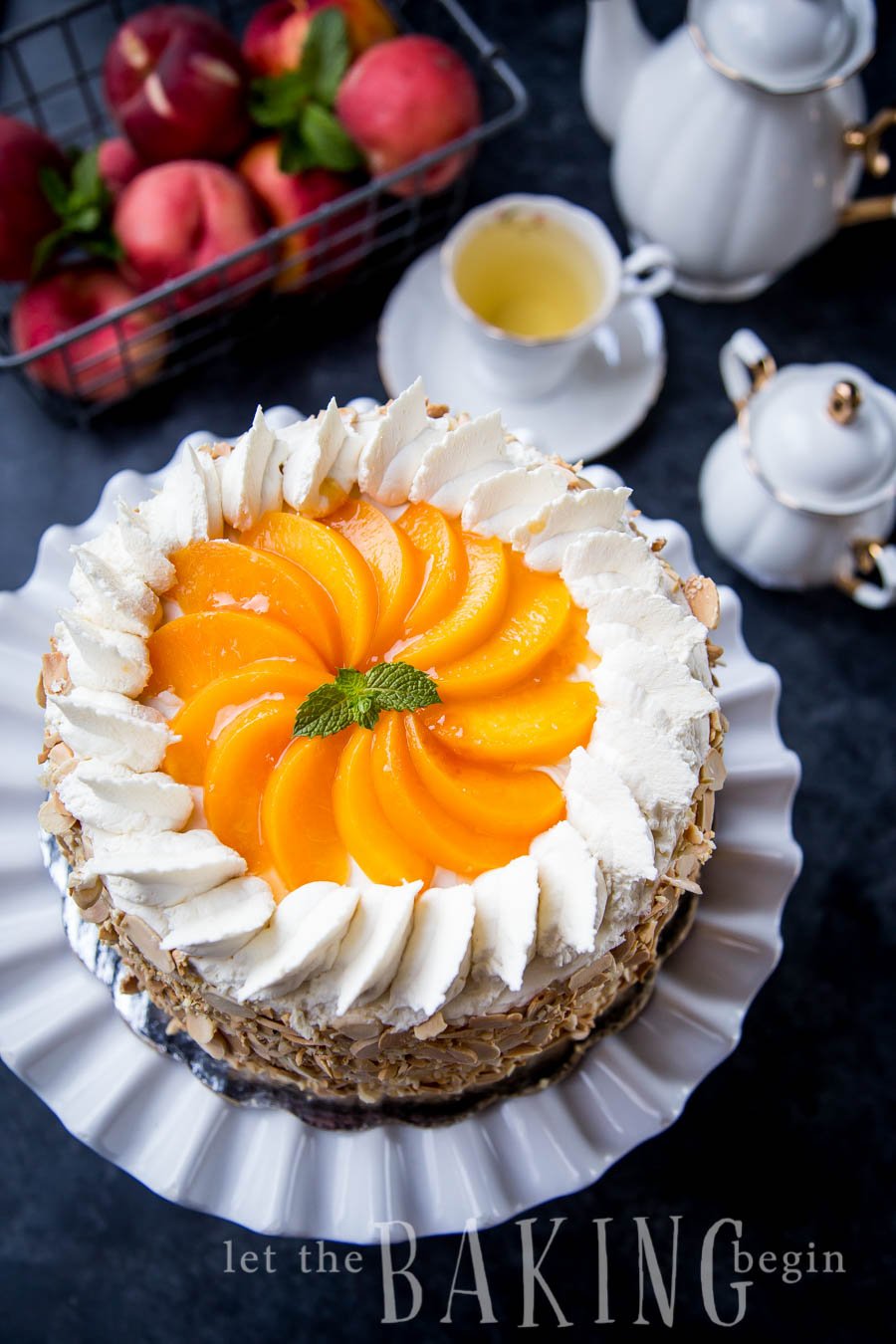 Peaches and cream cake on a cake platter next to a tea set. 