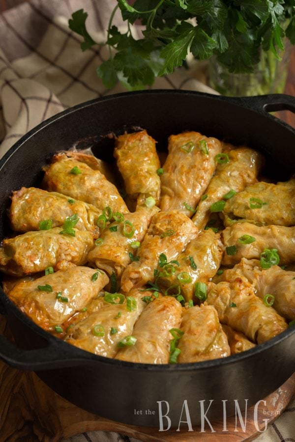 Stuffed cabbage rolls in a black cast iron pot topped with greens. 