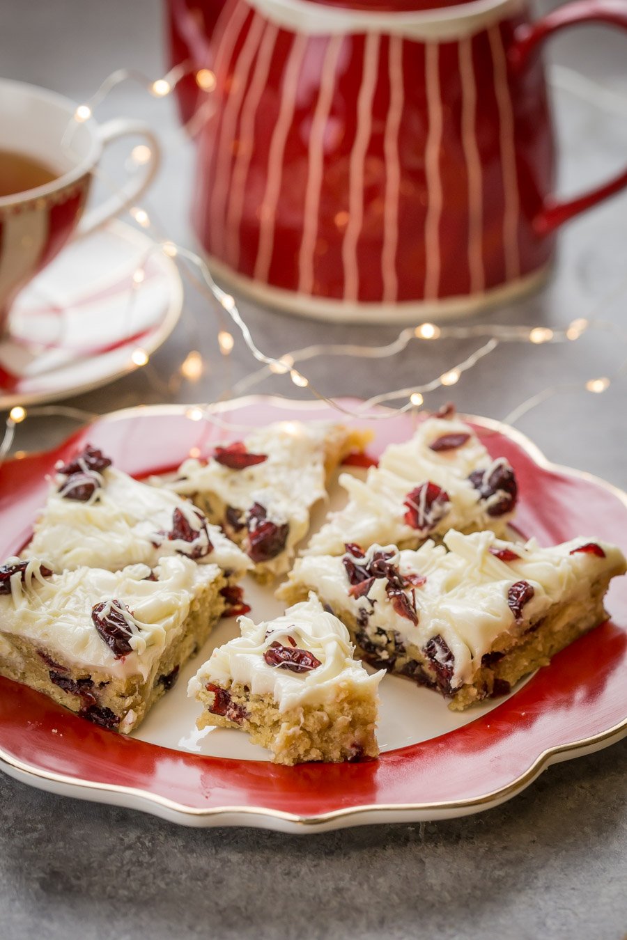 Cranberry Bliss Bars on a plate with a tea kettle next to it. 
