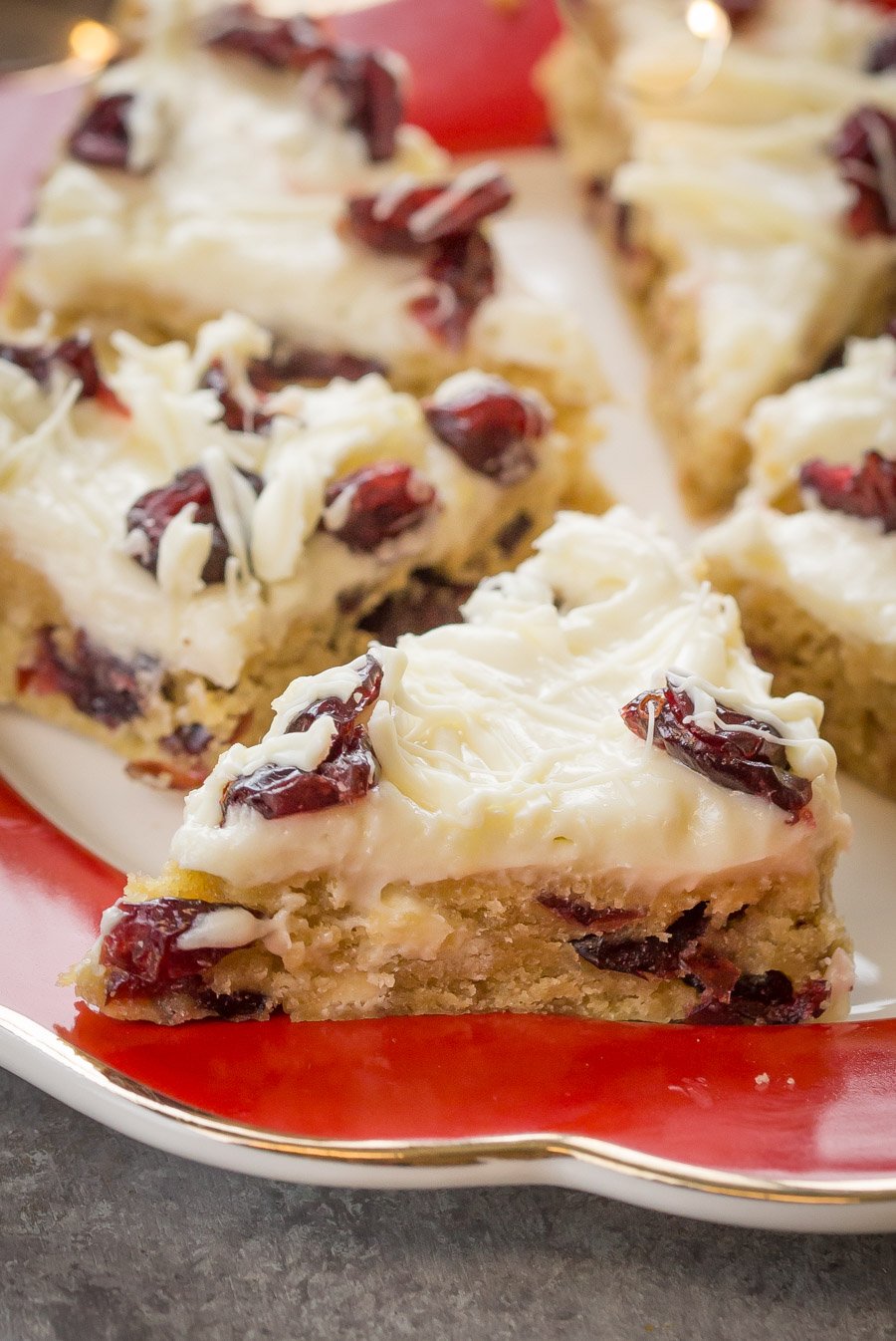 Cranberry Bliss Bars topped with a glaze and cranberries on a plate.