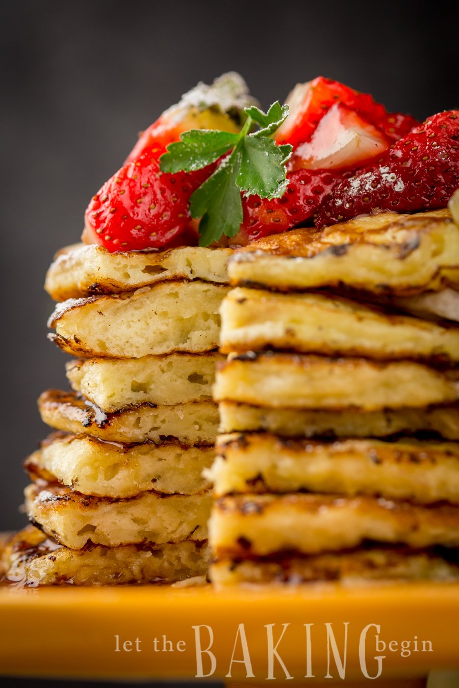 Sliceless stacked pancakes topped with fresh strawberries on a yellow platter. 
