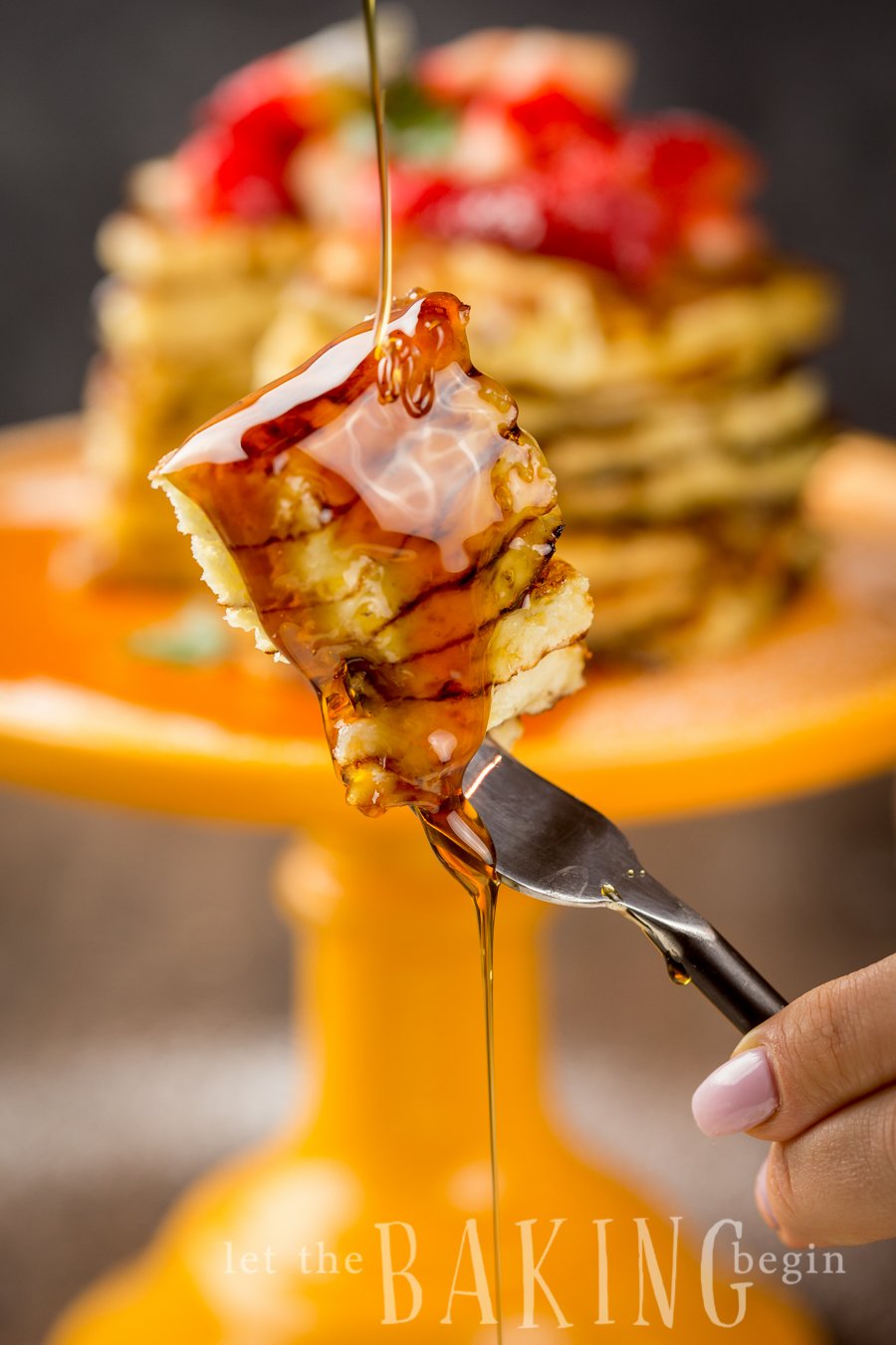 Slices of pancakes on a fork with maple syrup being poured on top. 