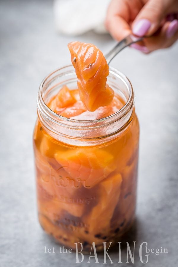 Salmon being pulled from mason jar of cured salmon and marinade.