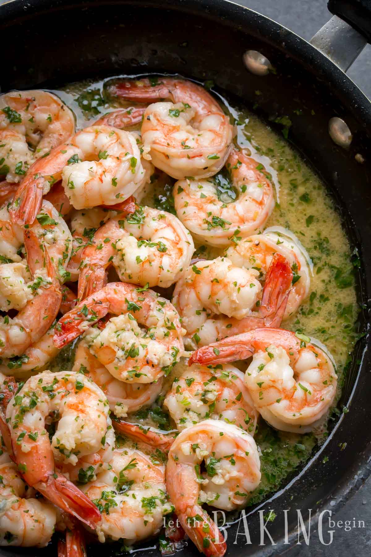 Cooked shrimp scampi with greens and butter in a skillet.