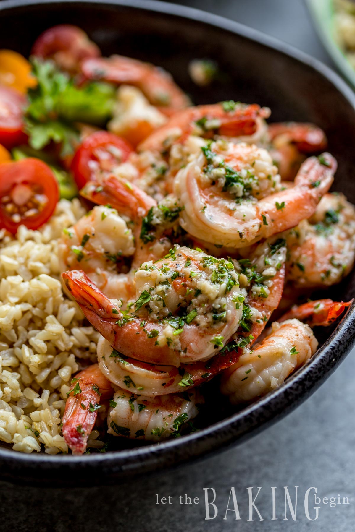 Close up picture of shrimp with fresh greens in a bowl with rice and tomatoes.