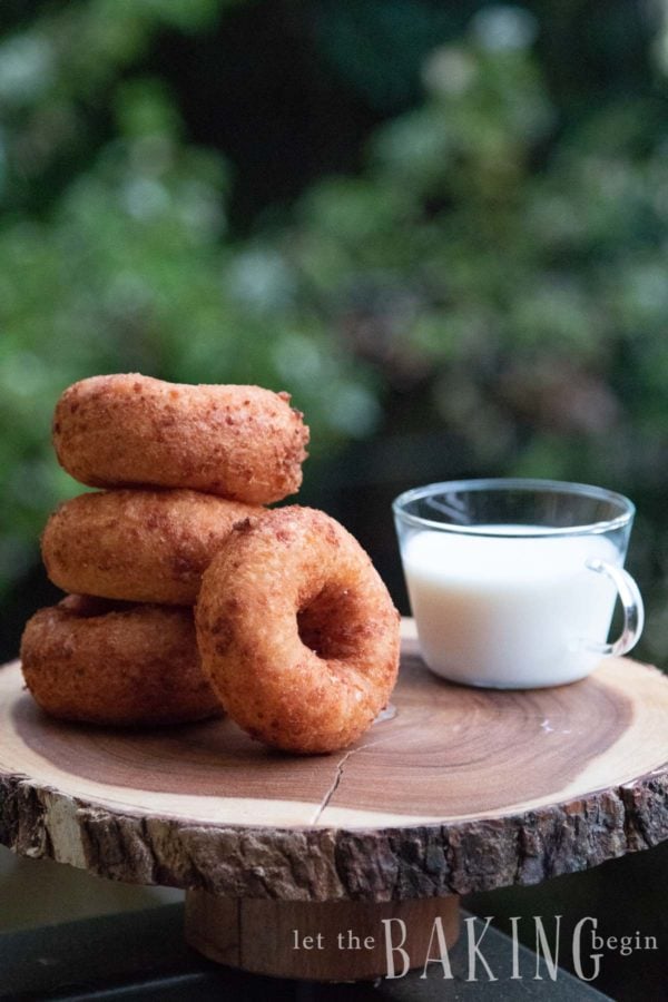 Quick Fried Donuts stacked on a board with a cup of milk in the back.