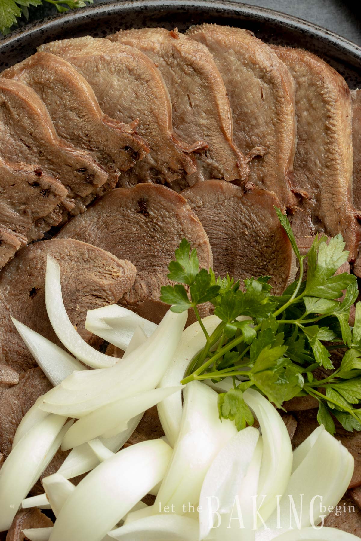 Beef recipes using cow tongue. Image of tongue sliced with herbs and onion. 