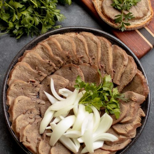 Sliced Beef Tongue on a plate with Onion and Herbs.