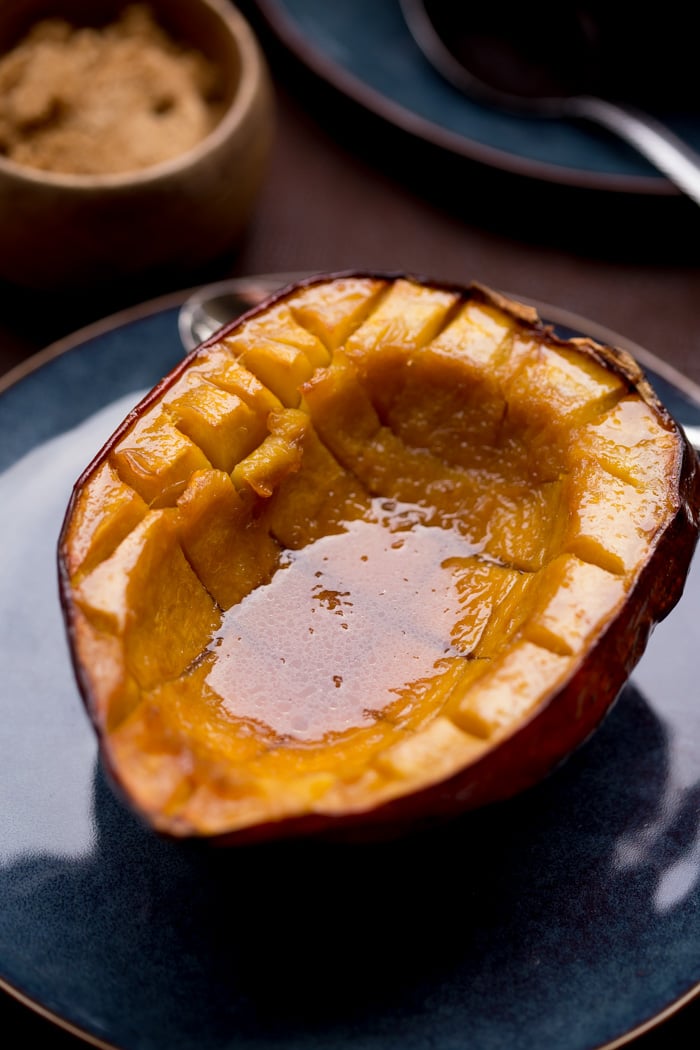 Half of Acorn Squash Baked with Brown Sugar and Butter on a plate, with lots of juice in the middle.