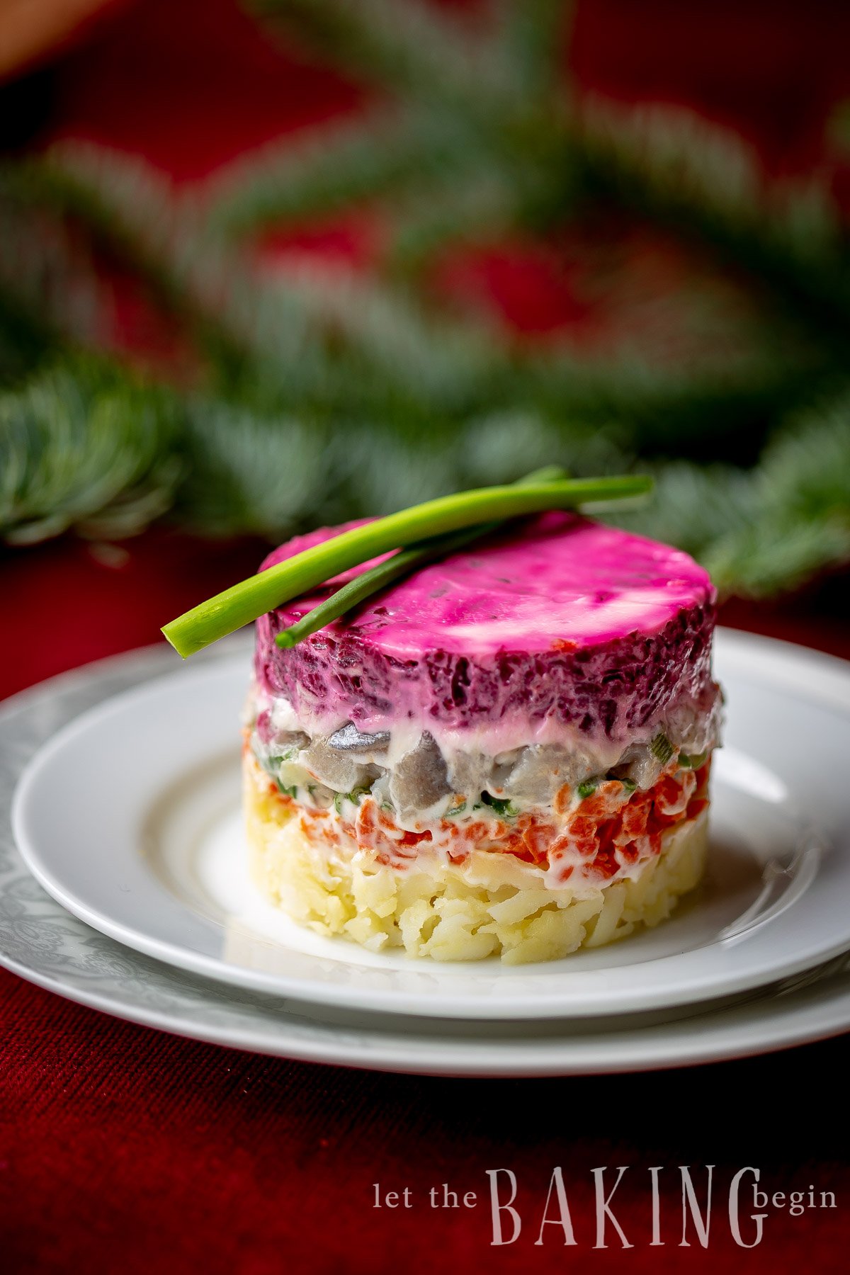 Layered beet salad topped with fresh greens on a white plate.