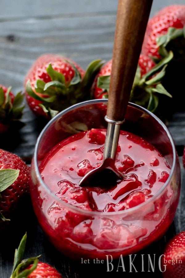Strawberry Topping in a glass with a spoon, surrounded by strawberries.