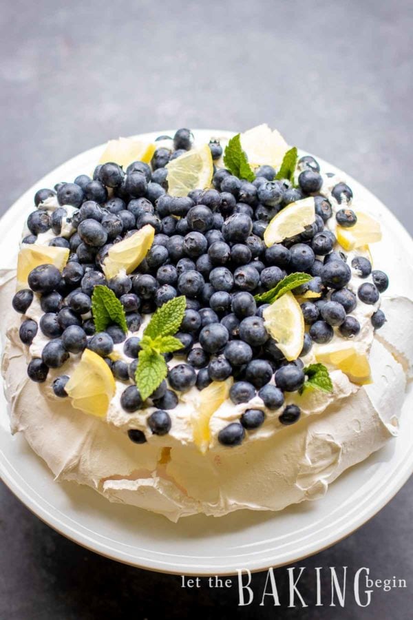 Pavlova cake topped with fresh cream, lemon wedges, blueberries and mint.