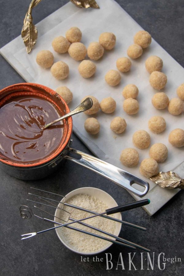 Coconut candy balls with bowl of melted chocolate next to them.